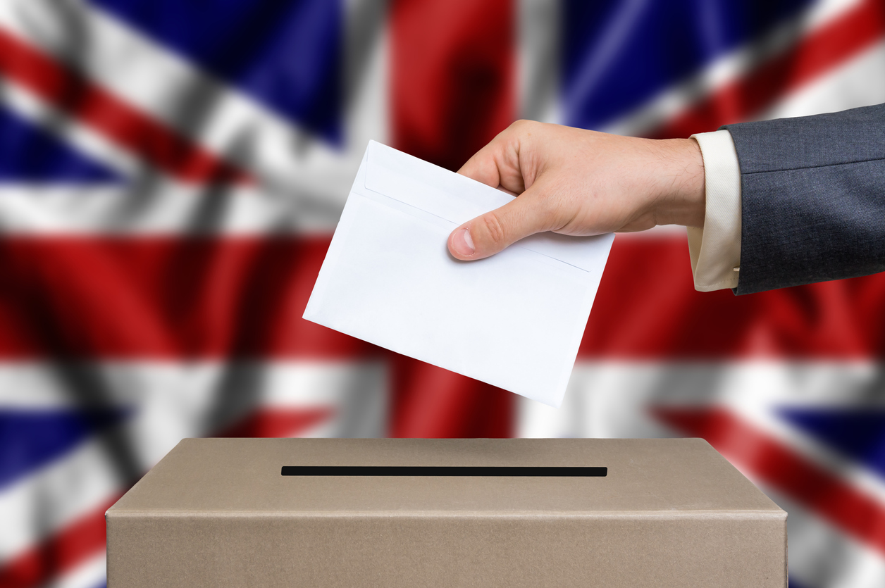 Election in Great Britain. The hand of man putting his vote in the ballot box. British flag on background.